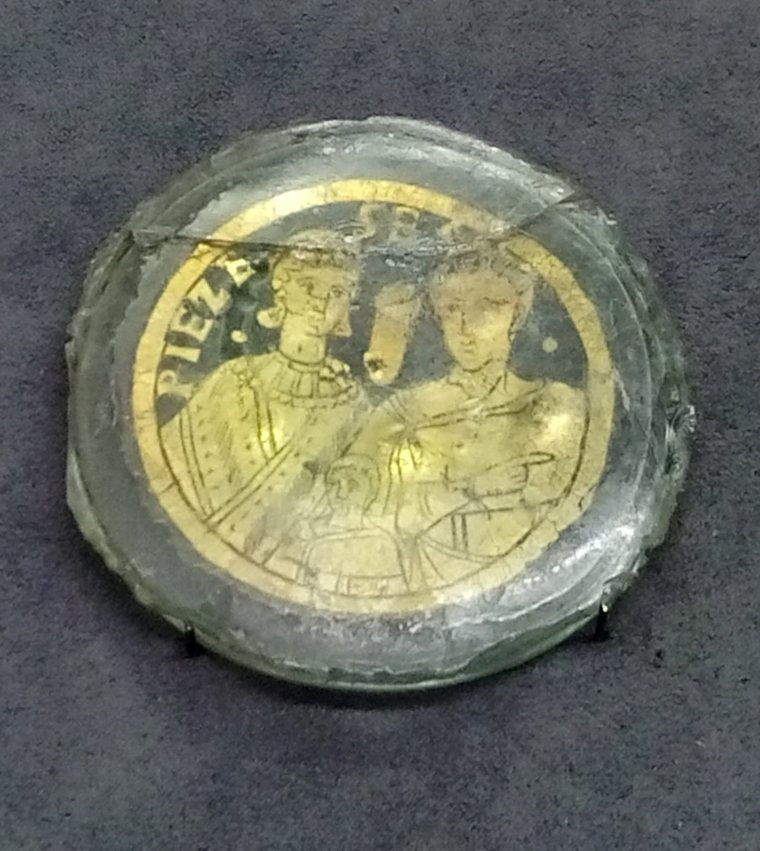 Medalhão de vidro com folha de ouro: um homem e uma mulher lado a lado e, entre eles, uma pequena figura que os coroa